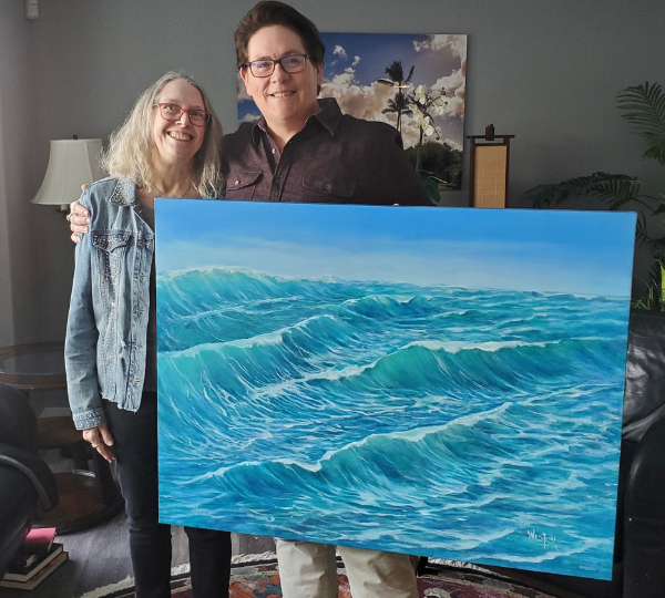 Two people holding a painting of blue ocean waves in a room.